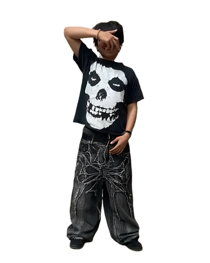 Person wearing black spider embroidered jeans with bold spider design and black graphic skull t-shirt