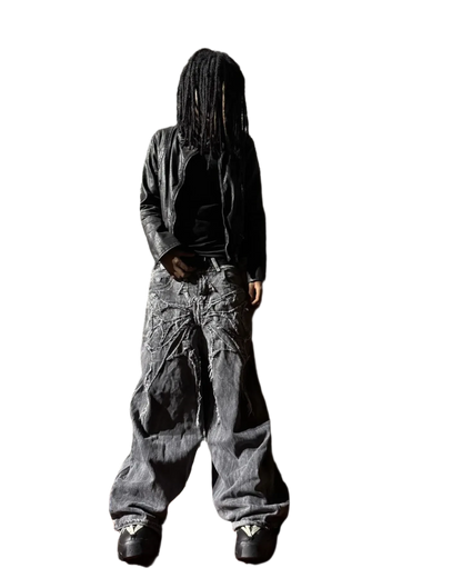 Person wearing spider embroidered jeans with black leather jacket and sneakers on black background